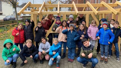 Schülerinnen und Schüler freuen sich gemeinsam mit ihrer Klassenlehrerin Adelheid Ammon über ihr Holz-Spielhaus, das vom Vorsitzenden der Regionalen PEFC-Arbeitsgruppe Hessen e. V., Detlef Stys übergeben wurde.