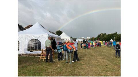 Montag Morgens, Schulen und Kindergärten besuchen die Kreistierschau Stände auf einer Wiese vor einem Regenbogen. Davor Schüler und Erwachsene.