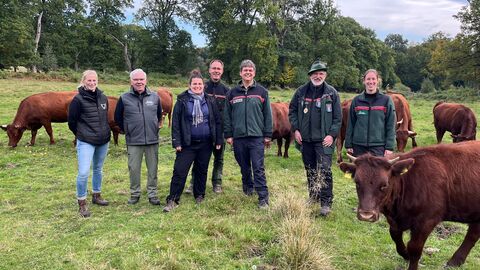 Eine Gruppe steht mit Hochlandrindern auf einer Wise und lächelt.