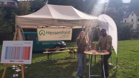 Zwei Menschen stehen vor einem Pavillon und Exponaten des Landesbetriebes HessenForst