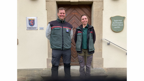 Zwei MEnschen in Forstdienstkleidung vor dem Forstamtsgebäude. 